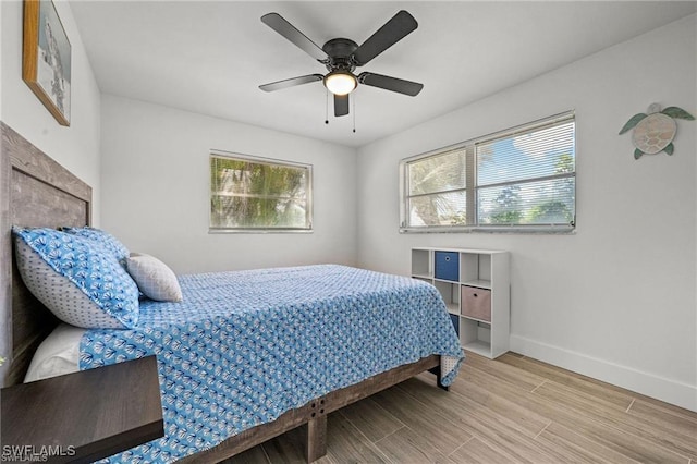 bedroom featuring a ceiling fan, multiple windows, baseboards, and wood finished floors