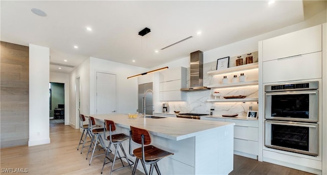 kitchen featuring wall chimney exhaust hood, modern cabinets, double oven, open shelves, and a sink