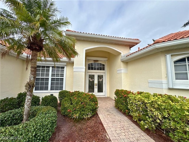 property entrance with french doors, a tile roof, and stucco siding