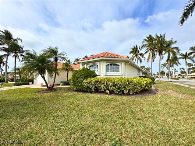 view of side of property with a tile roof, a yard, driveway, and stucco siding