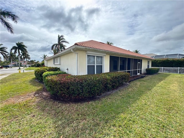 view of side of home with stucco siding, a tile roof, fence, and a yard