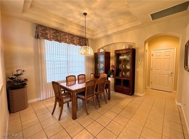 dining space with light tile patterned floors, arched walkways, and a raised ceiling