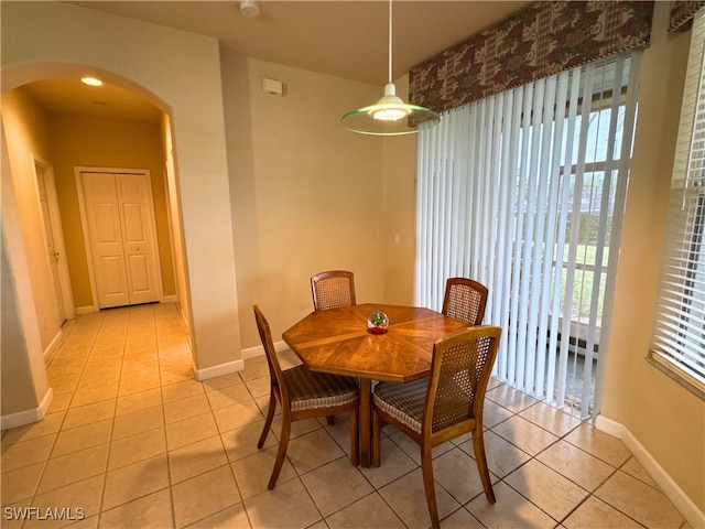 dining space featuring arched walkways, light tile patterned flooring, and a healthy amount of sunlight