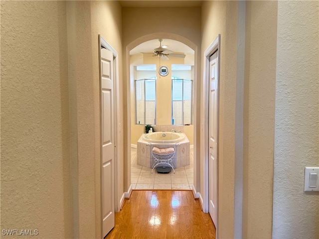 hallway with light wood-style floors, arched walkways, a textured wall, and a sink