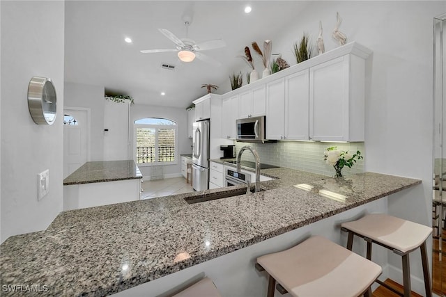 kitchen with stainless steel appliances, visible vents, decorative backsplash, stone countertops, and a sink