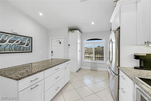 kitchen with light tile patterned floors, freestanding refrigerator, white cabinets, dark stone countertops, and baseboards