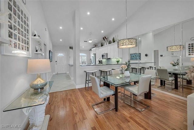 dining space featuring light wood-type flooring, baseboards, high vaulted ceiling, and a ceiling fan