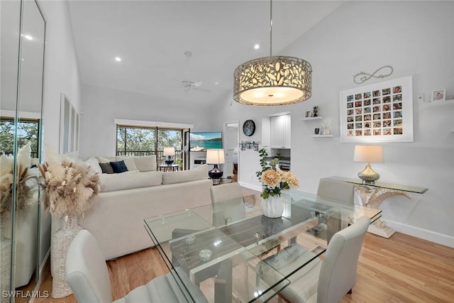 dining space with baseboards, ceiling fan, high vaulted ceiling, and wood finished floors