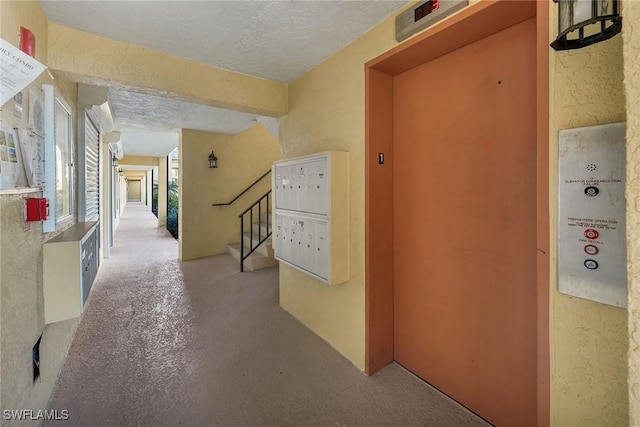 hall with elevator, a textured wall, a textured ceiling, and mail area