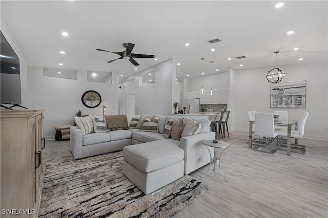 living room featuring visible vents, baseboards, light wood-style flooring, ceiling fan with notable chandelier, and recessed lighting