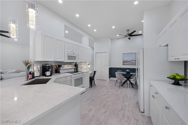 kitchen with light countertops, white cabinets, a sink, light wood-type flooring, and white appliances