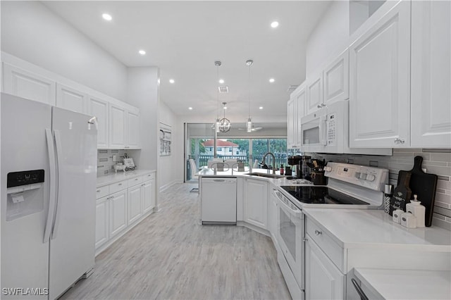 kitchen featuring white appliances, light wood finished floors, white cabinets, a peninsula, and a sink