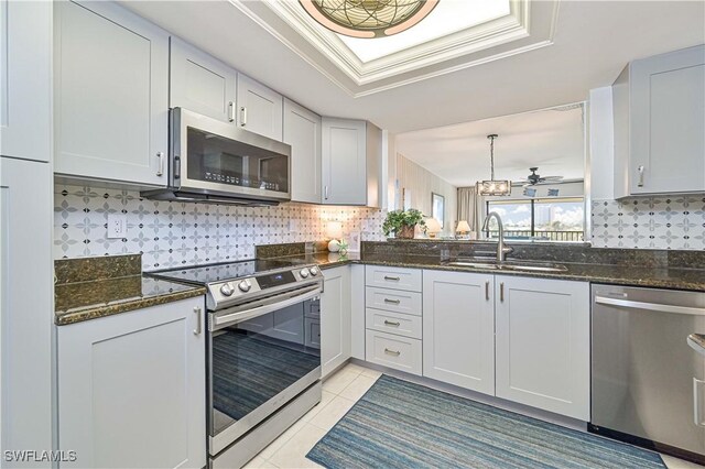 kitchen with light tile patterned floors, a sink, appliances with stainless steel finishes, a tray ceiling, and tasteful backsplash