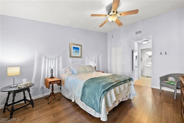 bedroom featuring visible vents, ensuite bath, baseboards, and wood finished floors