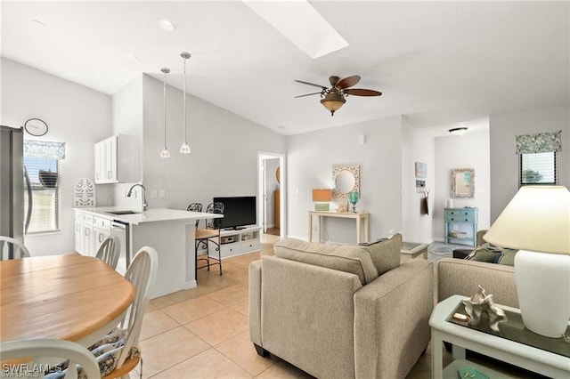 living area with a ceiling fan, vaulted ceiling with skylight, and light tile patterned flooring