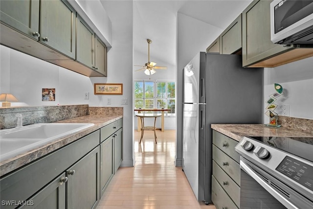 kitchen featuring stainless steel appliances, gray cabinets, light wood-style floors, a ceiling fan, and a sink