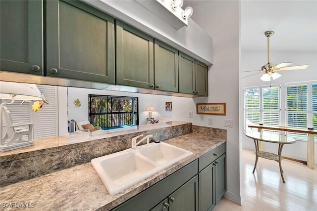 kitchen featuring a ceiling fan, a sink, light wood-style flooring, and green cabinets