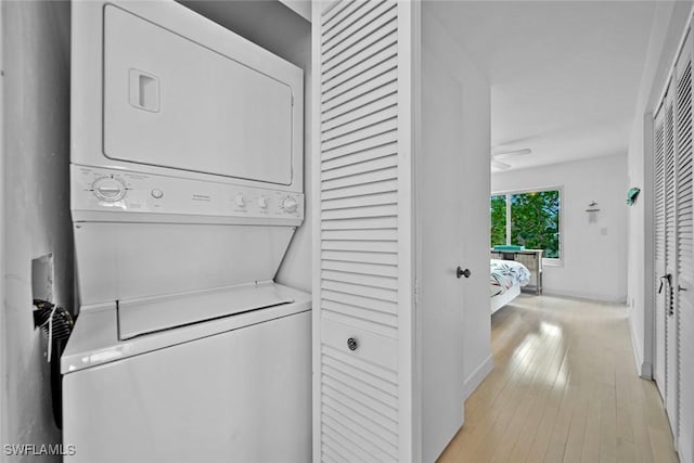 clothes washing area featuring laundry area, baseboards, light wood-style floors, and stacked washer and clothes dryer