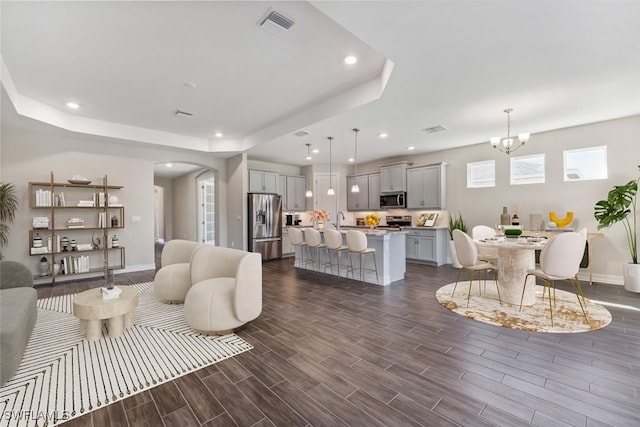 living area with wood finish floors, a raised ceiling, visible vents, and recessed lighting