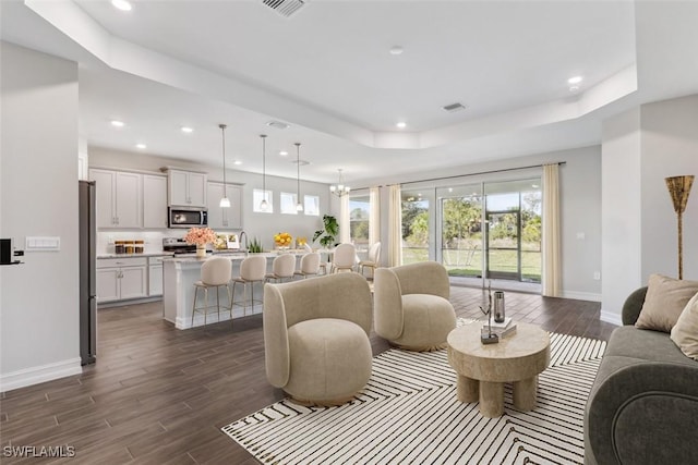 living room featuring a tray ceiling, dark wood-style flooring, recessed lighting, an inviting chandelier, and baseboards