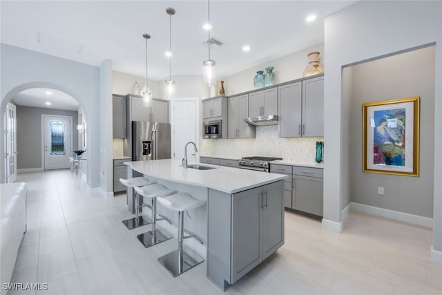 kitchen with arched walkways, appliances with stainless steel finishes, gray cabinets, under cabinet range hood, and a sink