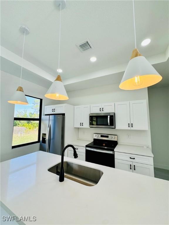 kitchen featuring stainless steel appliances, light countertops, visible vents, white cabinetry, and a sink