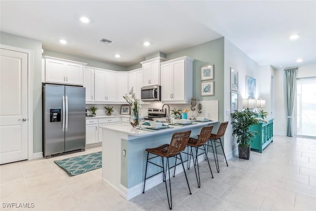 kitchen featuring visible vents, a breakfast bar area, a peninsula, stainless steel appliances, and white cabinetry