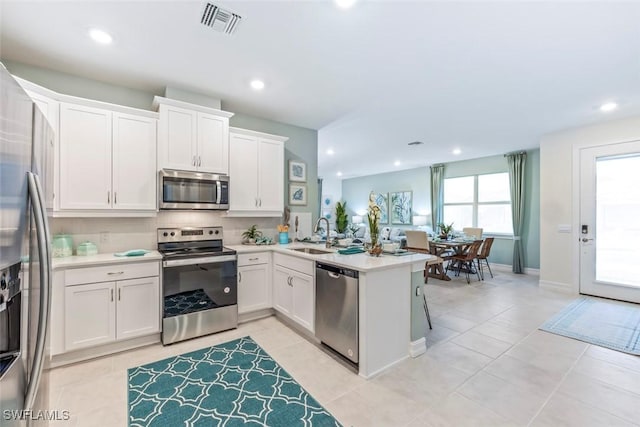 kitchen with appliances with stainless steel finishes, a peninsula, light countertops, white cabinetry, and a sink