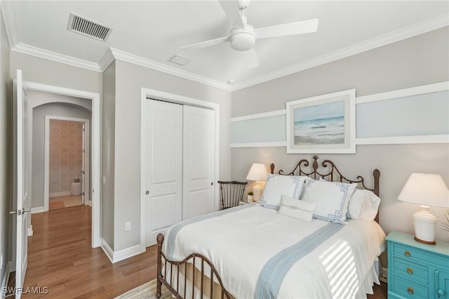 bedroom featuring crown molding, a closet, visible vents, wood finished floors, and baseboards