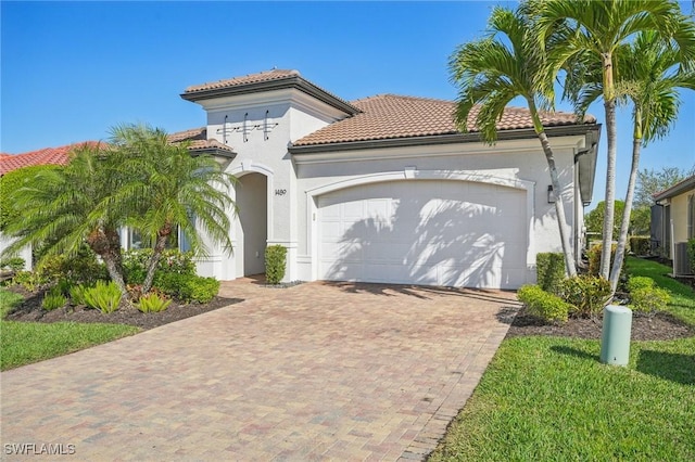 mediterranean / spanish-style house featuring cooling unit, a garage, a tile roof, decorative driveway, and stucco siding