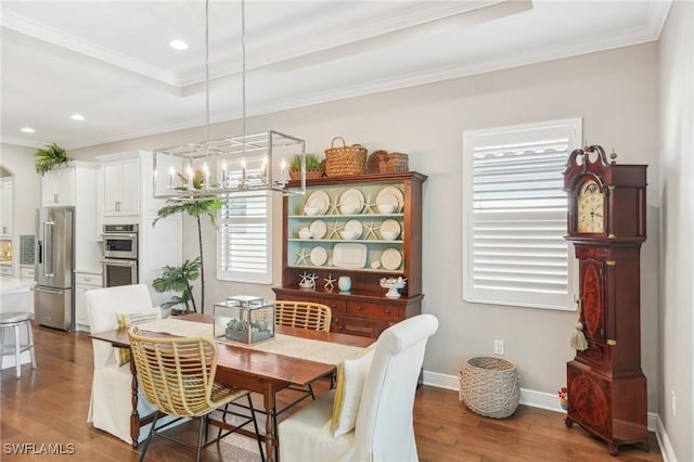 dining area with ornamental molding, a raised ceiling, baseboards, and wood finished floors