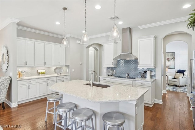 kitchen featuring arched walkways, black electric cooktop, a sink, visible vents, and wall chimney range hood