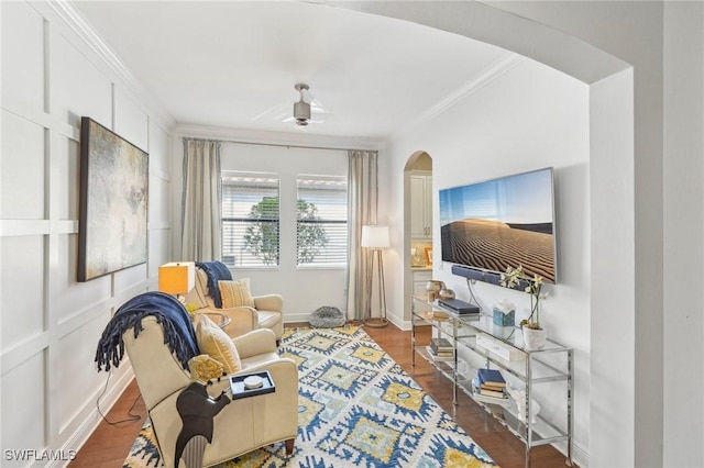 sitting room featuring baseboards, arched walkways, a decorative wall, and crown molding