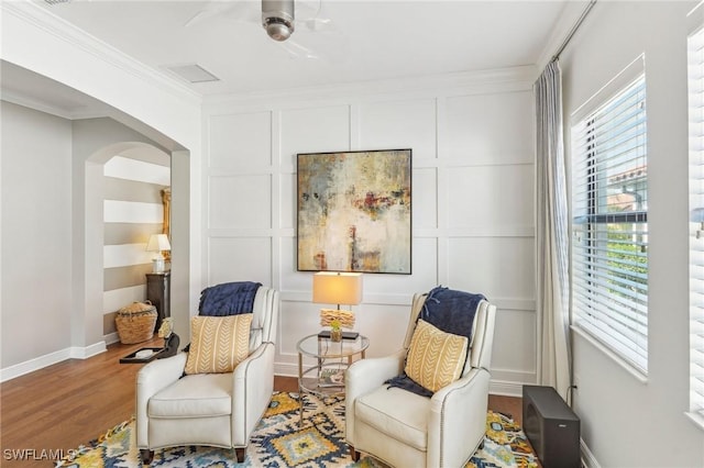 living area featuring arched walkways, a decorative wall, ornamental molding, wood finished floors, and baseboards