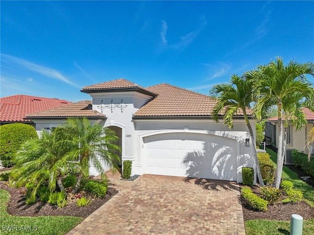 mediterranean / spanish house featuring an attached garage, a tile roof, decorative driveway, and stucco siding