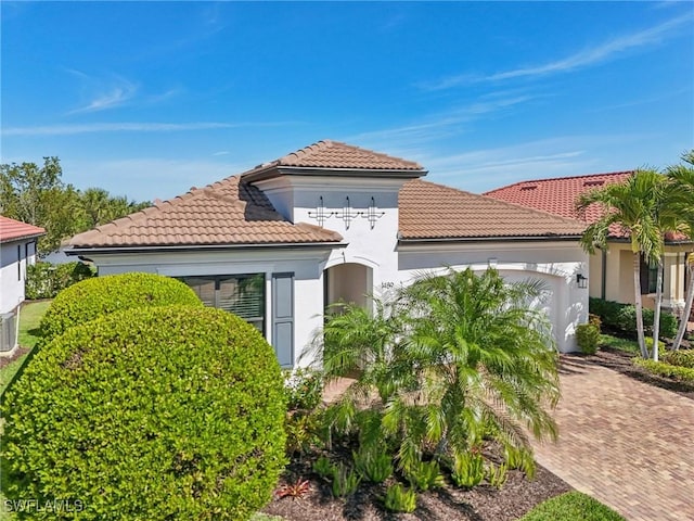 mediterranean / spanish-style house featuring decorative driveway, an attached garage, a tile roof, and stucco siding