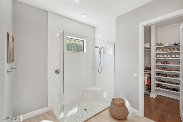 full bathroom featuring a walk in closet, a tile shower, baseboards, and wood finished floors