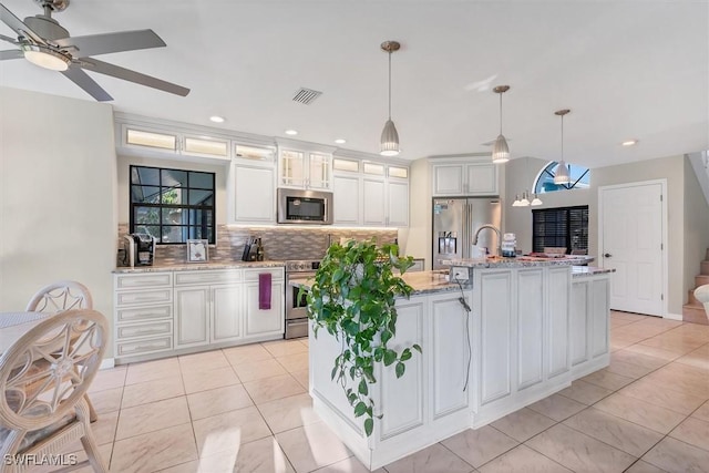 kitchen featuring visible vents, a center island with sink, backsplash, stainless steel appliances, and ceiling fan