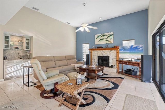 living area with light tile patterned floors, a stone fireplace, ceiling fan, and a towering ceiling