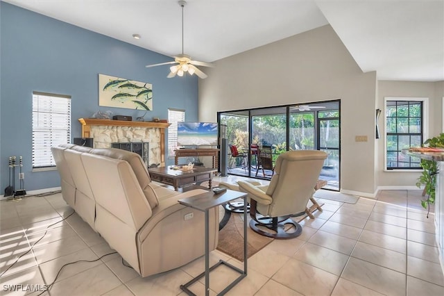 living area with ceiling fan, baseboards, light tile patterned floors, a fireplace, and a towering ceiling