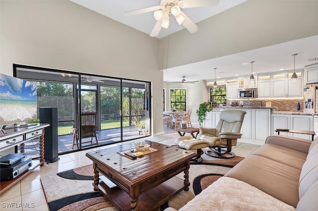 living area with a towering ceiling, light tile patterned flooring, and a ceiling fan