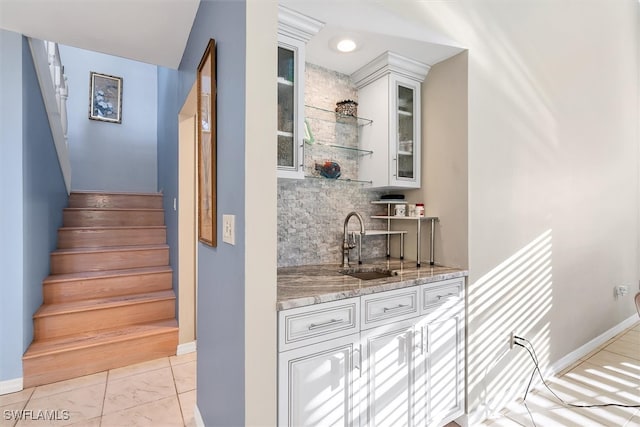 bar featuring baseboards, stairs, indoor wet bar, decorative backsplash, and a sink