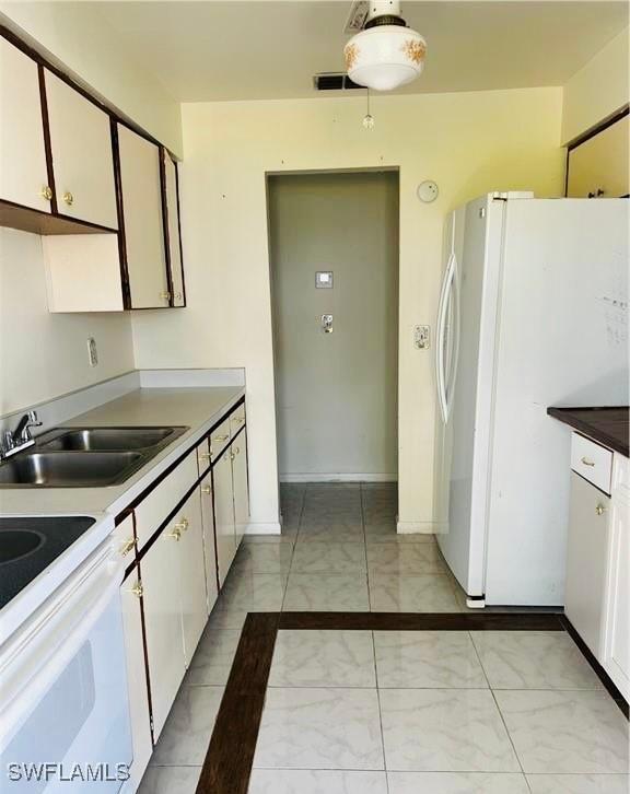 kitchen featuring white appliances, a sink, visible vents, white cabinets, and marble finish floor