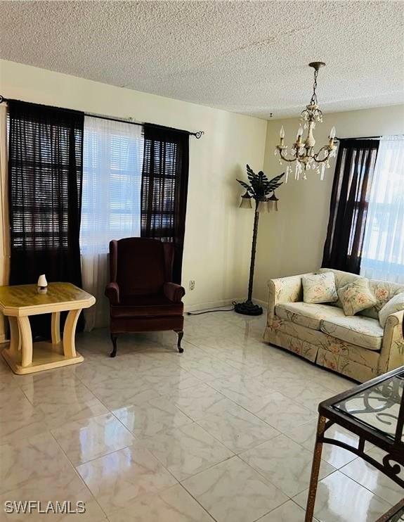 living area with marble finish floor, baseboards, a textured ceiling, and an inviting chandelier