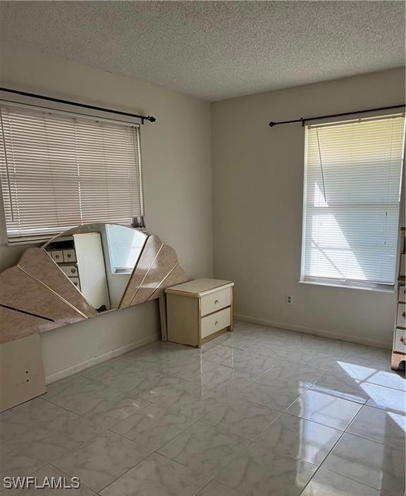 interior space with a textured ceiling, marble finish floor, and baseboards