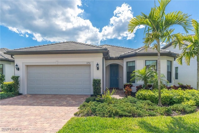 view of front of home with decorative driveway, a tile roof, an attached garage, and stucco siding