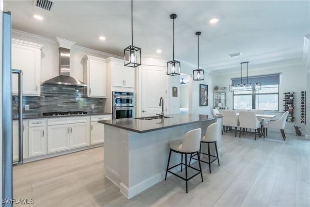 kitchen featuring stainless steel double oven, a sink, visible vents, wall chimney exhaust hood, and dark countertops