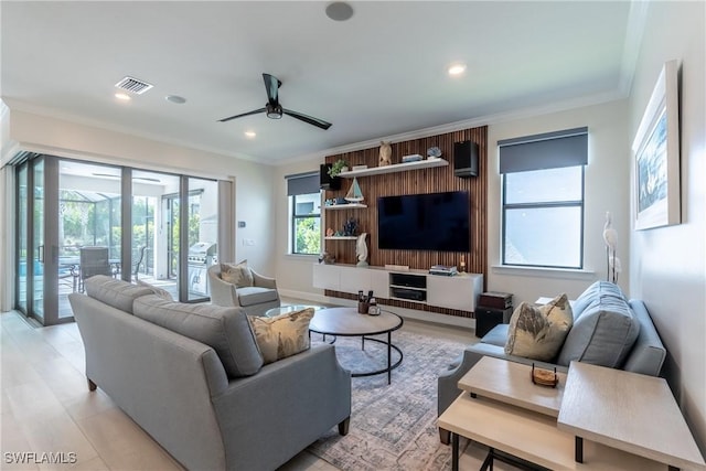 living area featuring ceiling fan, ornamental molding, light wood-type flooring, and visible vents