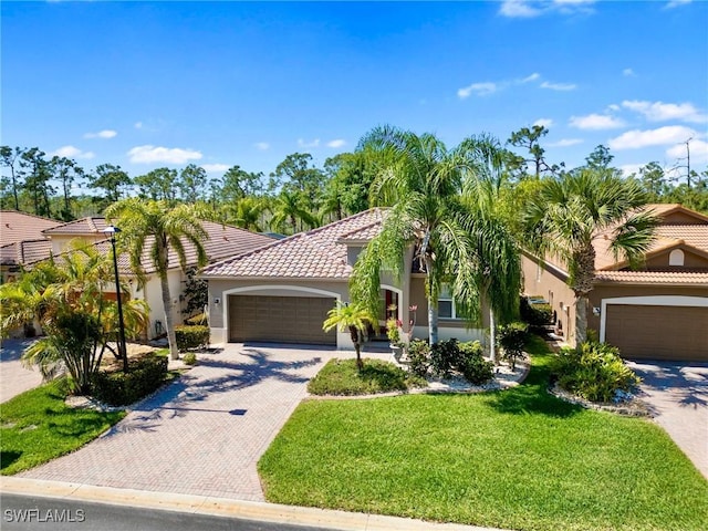 mediterranean / spanish home featuring a tile roof, an attached garage, decorative driveway, a front lawn, and stucco siding