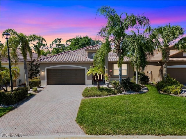 mediterranean / spanish-style home with a garage, stucco siding, a tiled roof, decorative driveway, and a front yard